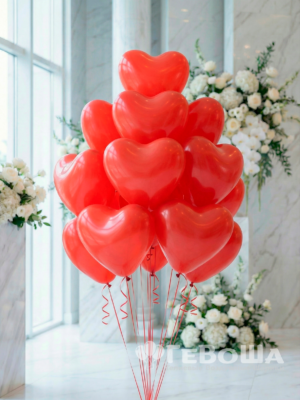 Букет красных латексных воздушных шаров в форме сердца с лентами в праздничном интерьере