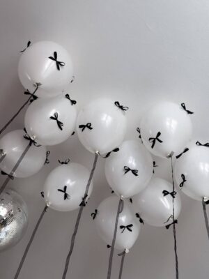 Белые перламутровые воздушные шары под потолком с черными декоративными бантиками и лентами.